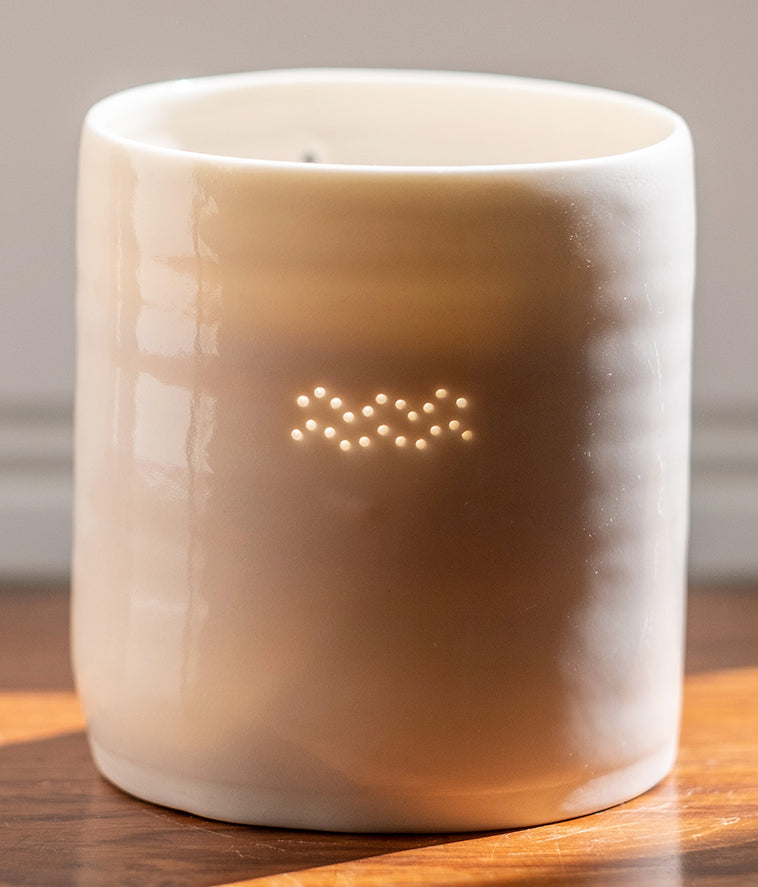 A ceramic porcelain tealight holder, with the Aquarius astrological symbol pierced into it with tiny holes, allowing candlelight to twinkle through. It has natural glossy glaze and is almost translucent.