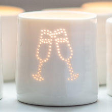 Load image into Gallery viewer, A porcelain ceramic tealight candle holder, votive, with a design of two clinking champagne glasses. Natural glossy glaze. Celebration. Party. Engagement. Wedding. Anniversary gift.