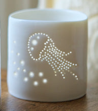 Load image into Gallery viewer, Porcelain candle holder with delicate jellyfish design pierced into it. Candlelight flickers through the holes. Ceramic tealight holder for seaside holidays.