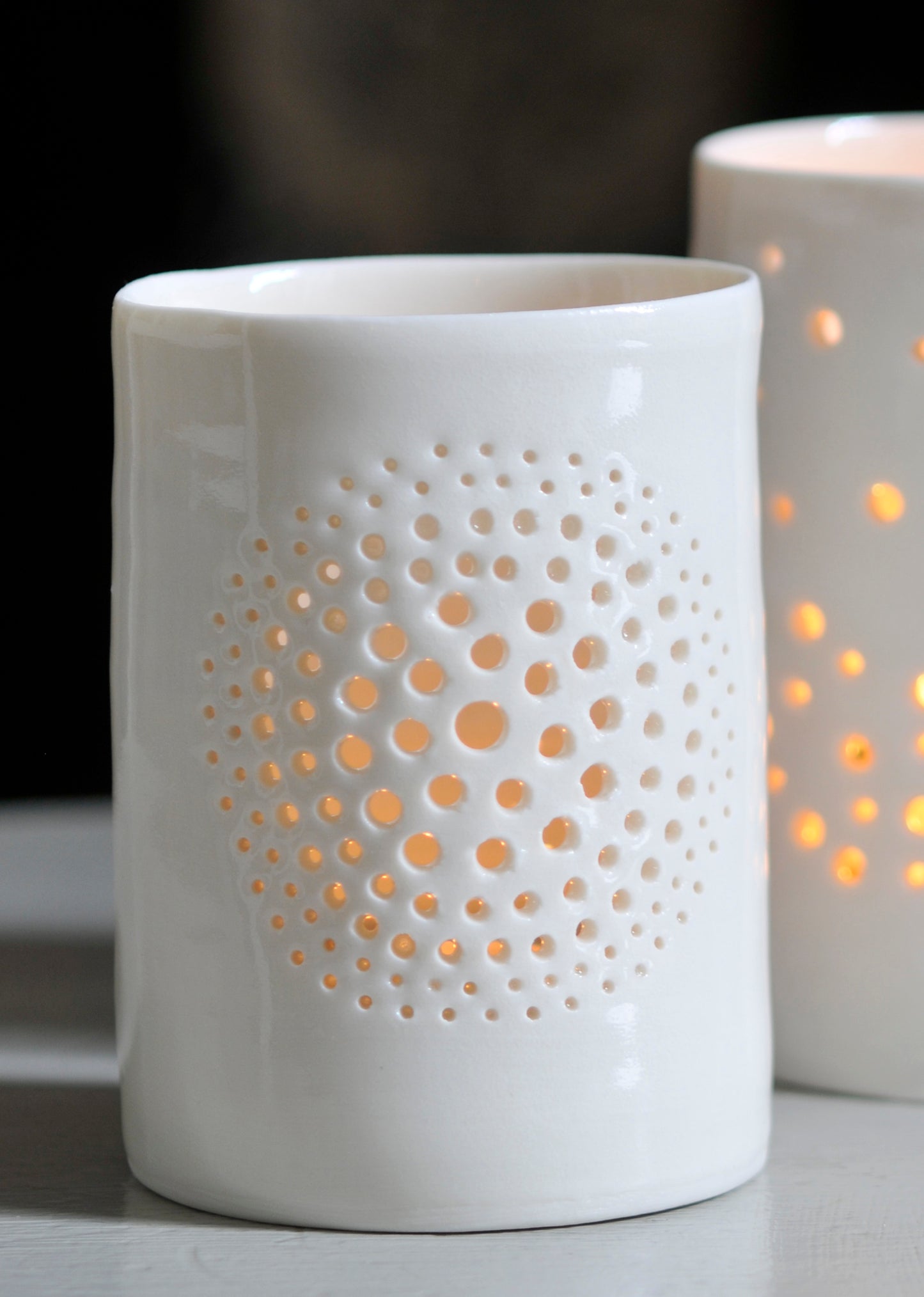 A natural porcelain ceramic tealight candle holder, with a floral design, resembling a large flower, like a dandelion. Homeware and garden decoration. Porcelain tableware. Candlelit glow.