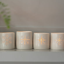 Load image into Gallery viewer, Line-up of four porcelain ceramic tealight candle holders, glazed in a natural glossy glaze, and pierced with different snowflake designs. Christmas gift. Decoration.