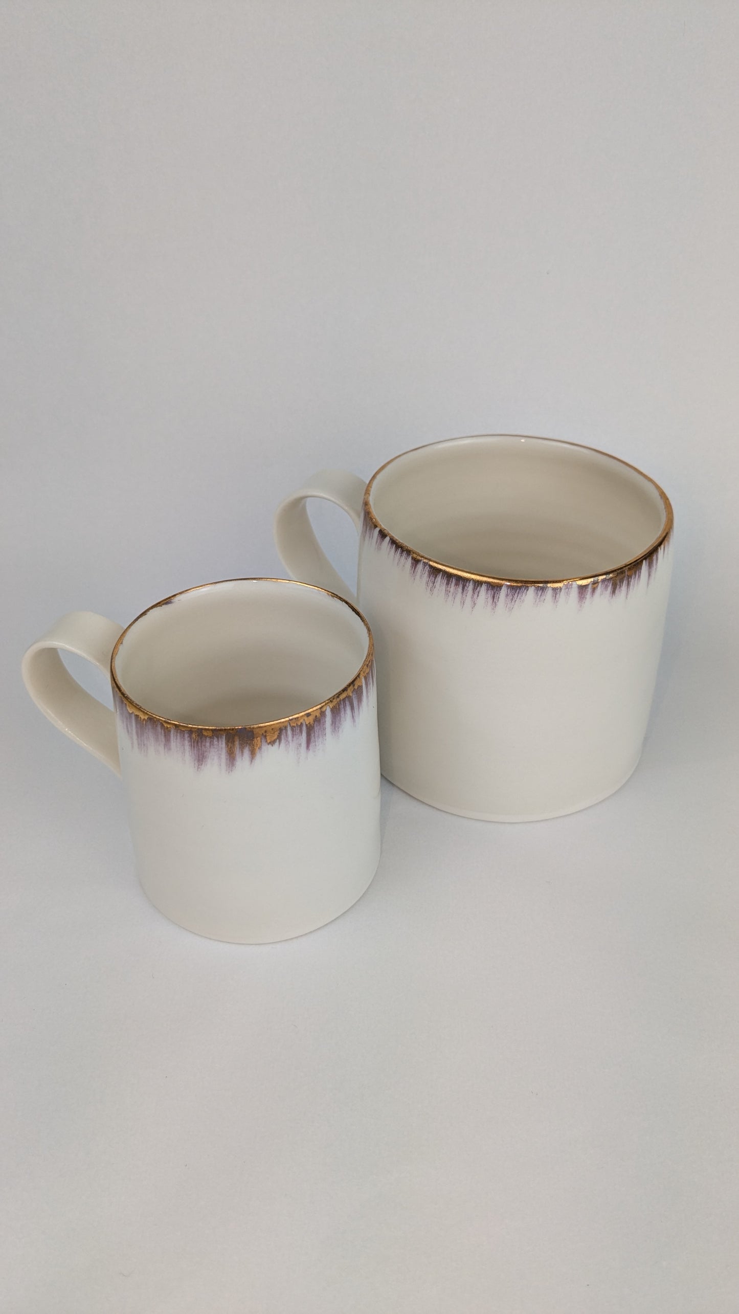 Two ceramic mugs with gold rim on a white background
