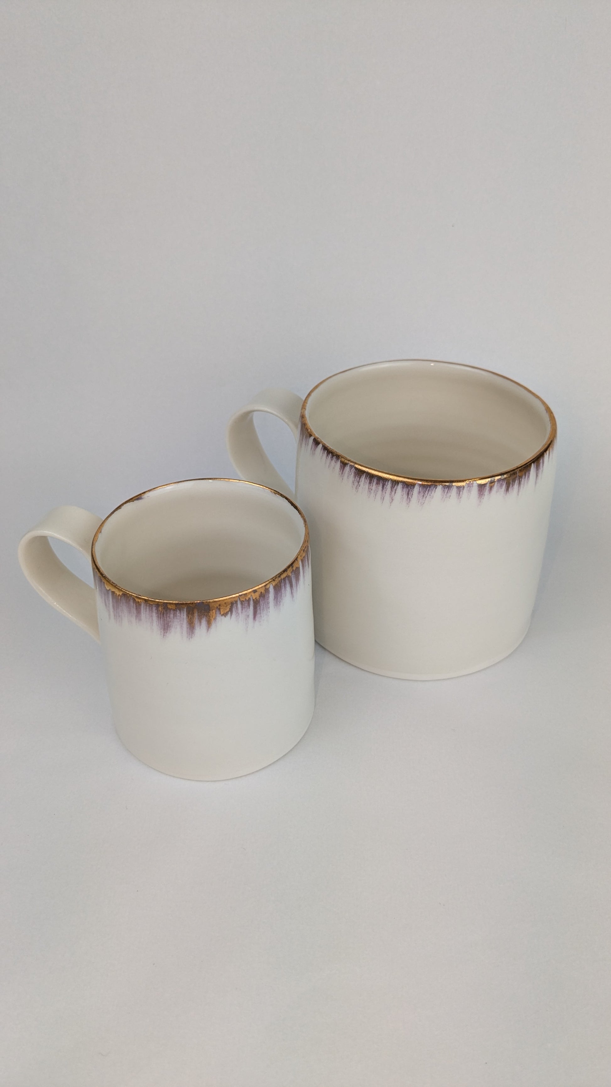 Two ceramic mugs with gold rim on a white background