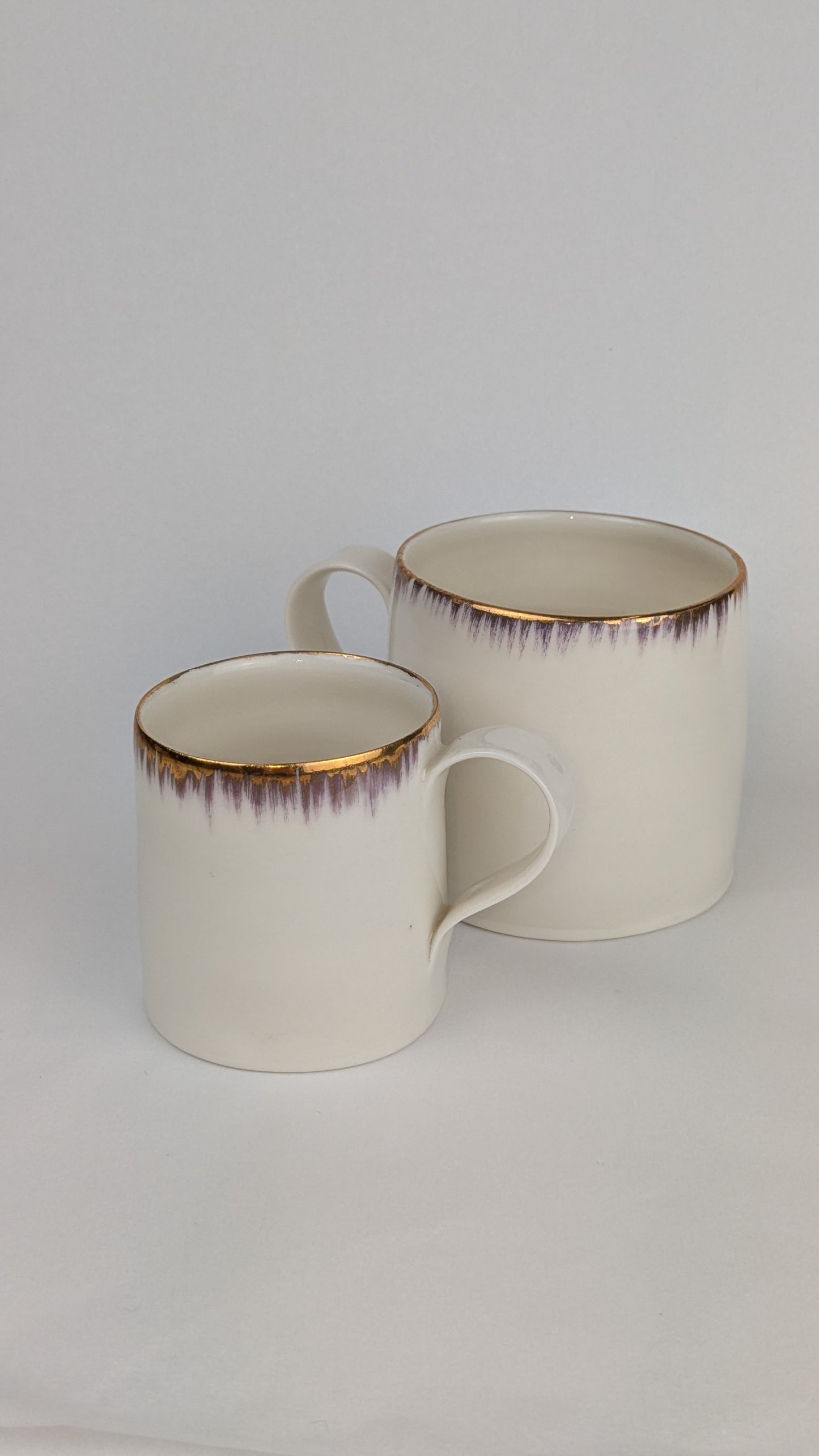 Two ceramic mugs with rimmed edges on a light gray background
