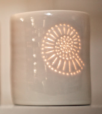 A ceramic porcelain tealight candle holders, featuring a delicately pierced ammonite fossil shell design, that the candlelight twinkles through. Homeware for relaxing and creating a calm atmosphere.