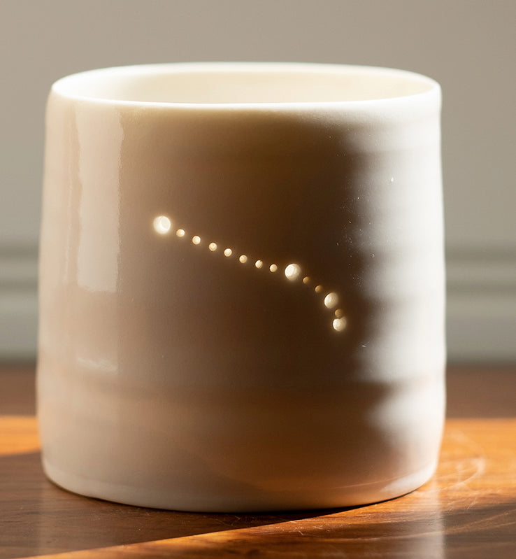 A ceramic porcelain tealight holder, with the Aries astrological constellation pierced into it with tiny holes, allowing candlelight to twinkle through. The tealight holder has natural glossy glaze and is almost translucent. Relaxing homeware.