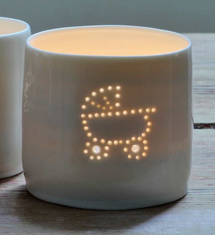 Porcelain ceramic tealight candle holder, glazed in a natural glossy glaze, and pierced with a baby pram design. New baby gift.