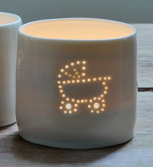 Porcelain ceramic tealight candle holder, glazed in a natural glossy glaze, and pierced with a baby pram design. New baby gift.