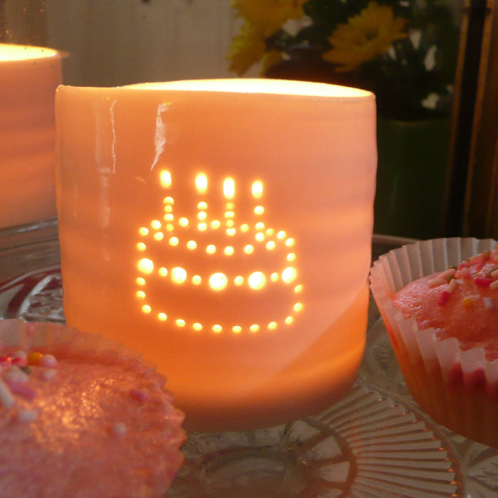 Porcelain ceramic tealight candle holder, featuring a design of a birthday cake with candles, natural glossy glaze. Sitting next to two cupcakes. Birthday present. Celebration.