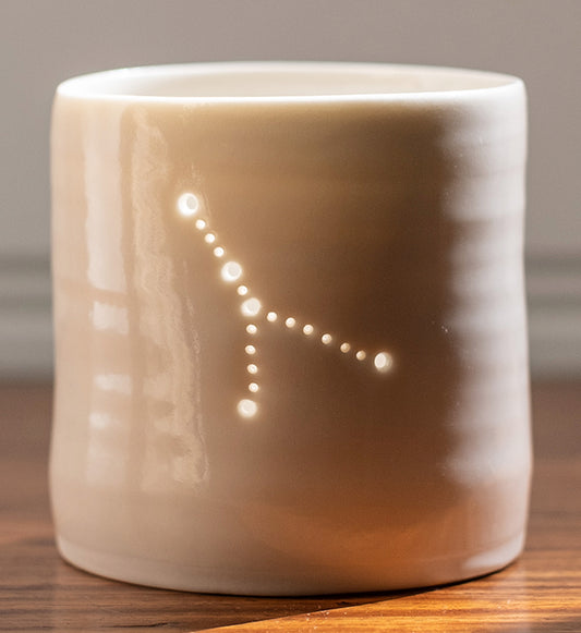 A ceramic porcelain tealight holder, with the Cancer astrological constellation pierced into it with tiny holes, allowing candlelight to twinkle through. Natural glossy glaze, almost translucent. Horoscope, astrology, zodiac.