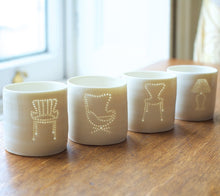Load image into Gallery viewer, A line-up of four porcelain ceramic tealight candle holders, showing classic design midcentury furniture, including chairs and lamps
