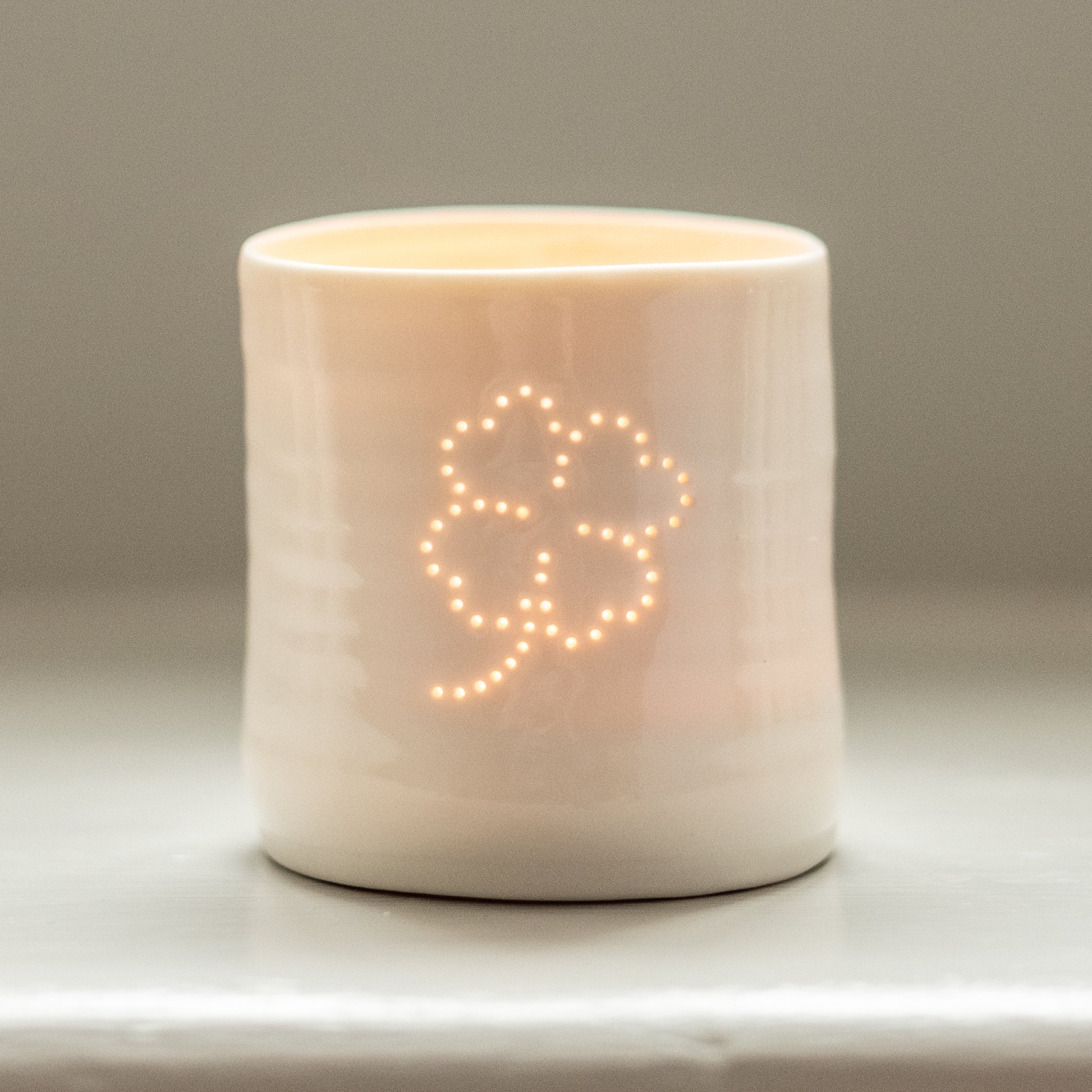 Ceramic porcelain tealight candle holder, featuring a design of a lucky four leafed clover. Tiny holes let the light shine through.