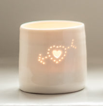 Load image into Gallery viewer, A ceramic porcelain tealight holder, with a cupids heart pierced into it with tiny holes, allowing candlelight to twinkle through. The tealight holder has natural glossy glaze and is almost translucent. Relaxing homeware. Romantic gift.
