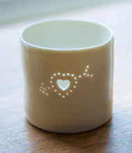 Load image into Gallery viewer, A cute ceramic porcelain tealight holder, with a cupids heart pierced into it. There are small holes, that let candlelight shine through. Natural glossy glaze, almost translucent. Relaxing homeware. Romantic gift.
