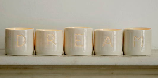 A series of five handmade porcelain tealight holders. These ceramic candle holders spell out the word "dream". Small business. Relaxing candles.