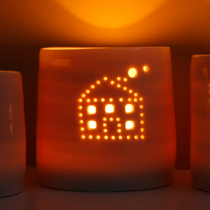 A cute house with smoke emerging from the chimney, pierced into a ceramic porcelain tealight candle holder. This candle votive will create a sense of home, hygge and warmth. Glowing from within.