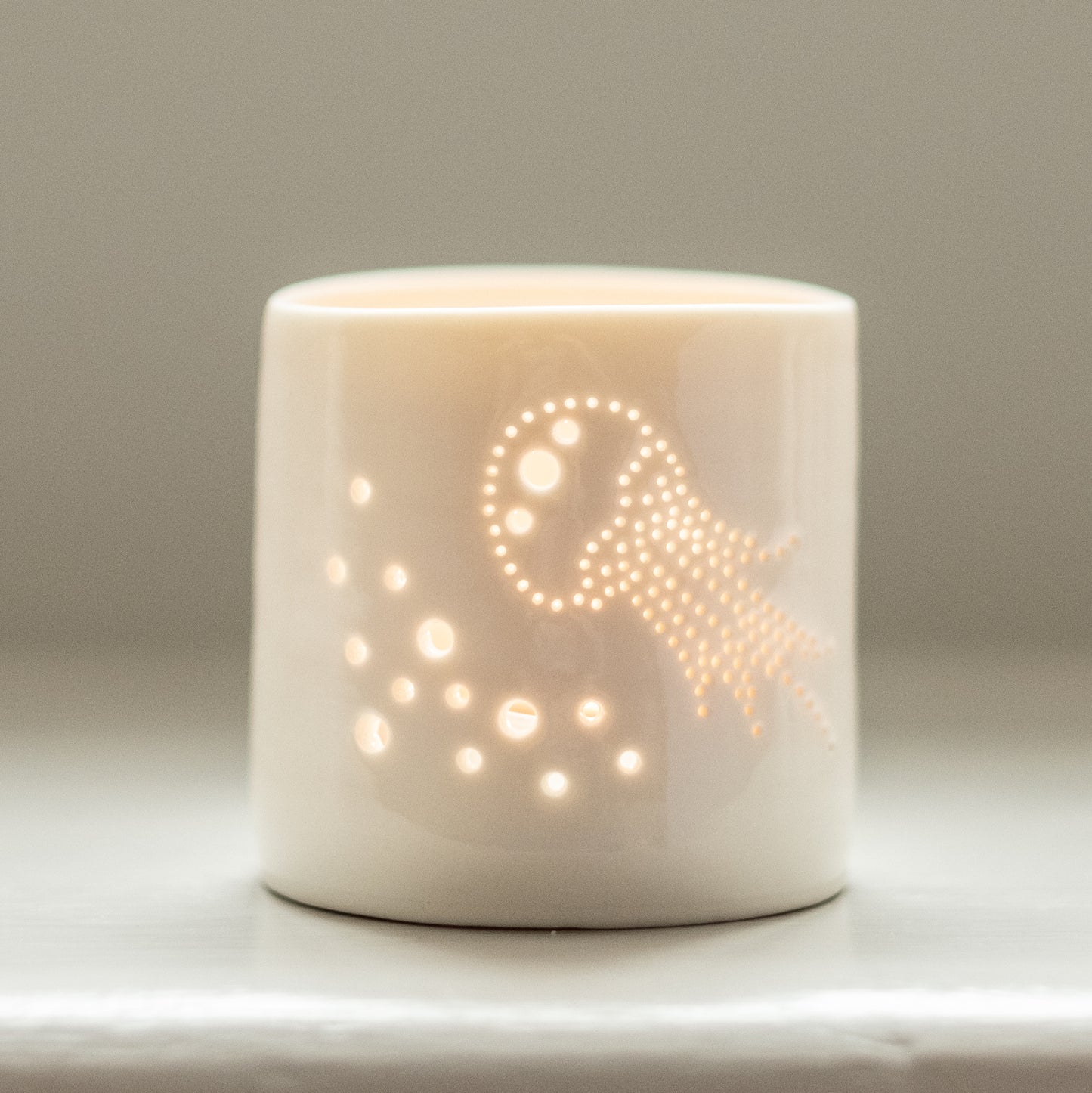Porcelain candle holder with delicate jellyfish design pierced into it. Candlelight flickers through the holes. Ceramic tealight holder for seaside holidays.