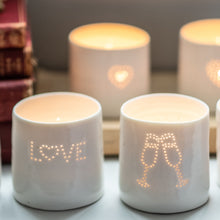 Load image into Gallery viewer, Two porcelain ceramic tealight candle holders, votive, with a design of two clinking champagne glasses, and the word LOVE. Natural glossy glaze. Celebration. Party. Engagement. Wedding. Anniversary gift.
