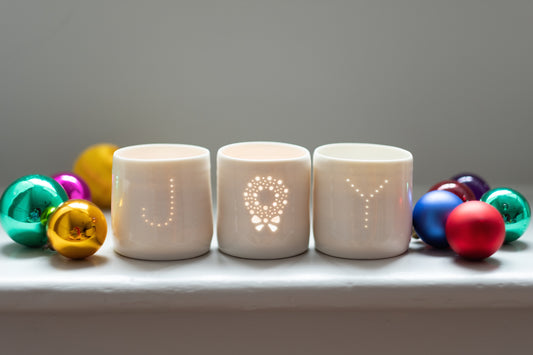 A set of three ceramic candle holders spelling out the word JOY, with a Christmas wreath replacing the O. Simple scandi candles to create a sense of hygge.