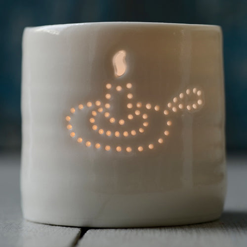 A porcelain ceramic tealight candle holder, votive, with an old fashioned candle holder design pierced into it using tiny holes. Natural glossy glaze. Homeware.