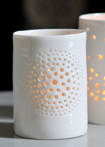 A natural porcelain ceramic tealight candle holder, with a floral design, resembling a large flower, like a dandelion. Homeware and garden decoration. Porcelain tableware. Candlelit glow.