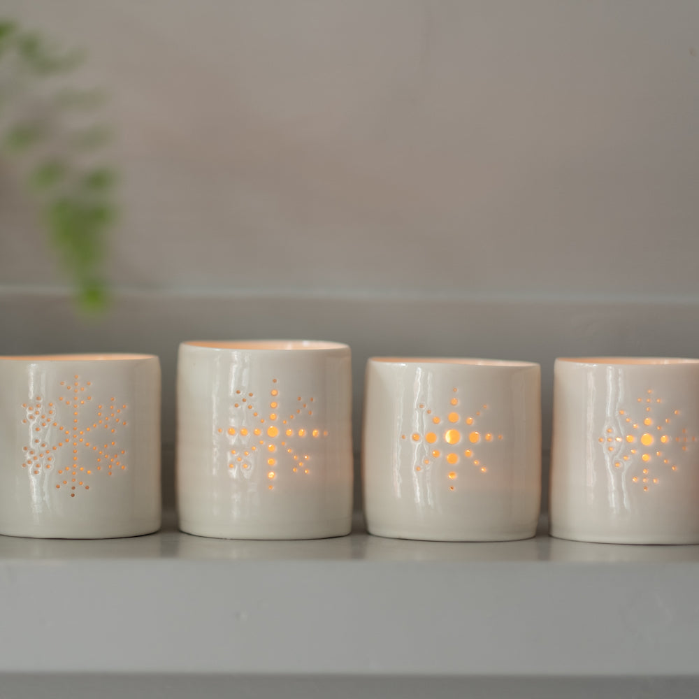 Line-up of four porcelain ceramic tealight candle holders, glazed in a natural glossy glaze, and pierced with different snowflake designs. Christmas gift. Decoration.