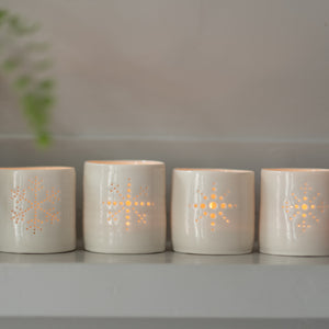 Line-up of four porcelain ceramic tealight candle holders, glazed in a natural glossy glaze, and pierced with different snowflake designs. Christmas gift. Decoration.