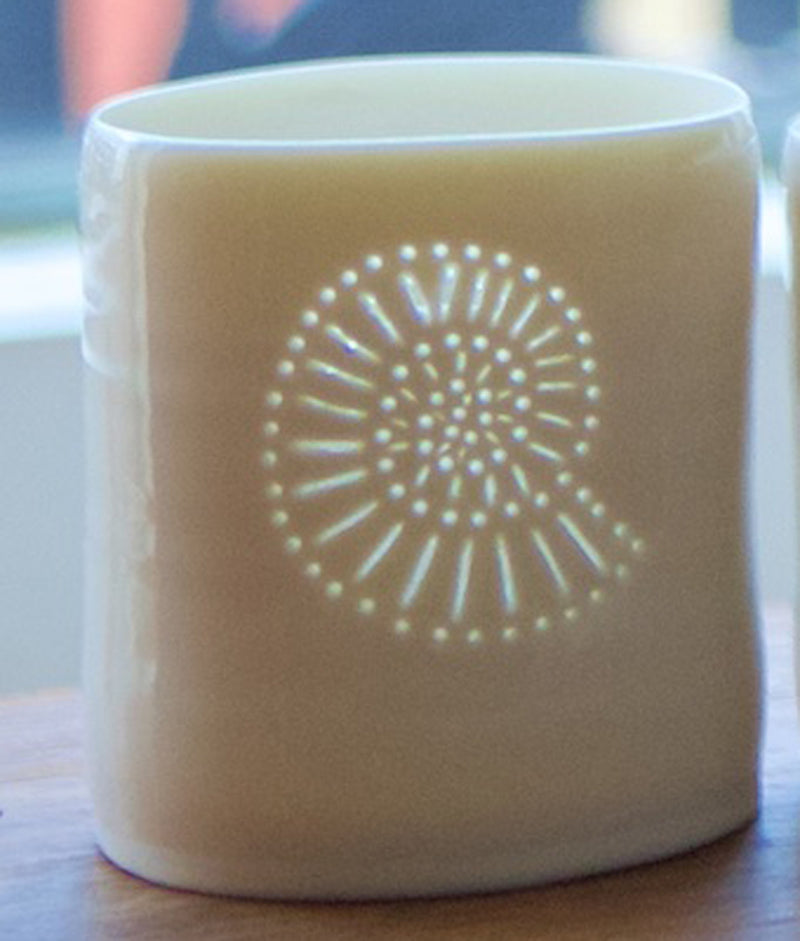 A photo of a ceramic porcelain tealight candle holder featuring a delicately pierced ammonite fossil design