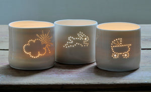 Trio of porcelain ceramic tealight candle holders, glazed in a natural glossy glaze, and pierced with different designs. One is a baby pram, one is a cloud with the sun peeping through, and one is a bunny. New baby gift.